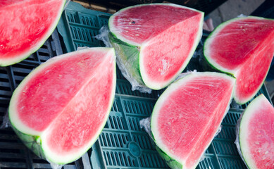 Close-up view of fresh ripe watermelon slices wrapped in plastic film and displayed on black and...