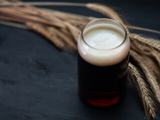 Dark ale glass on dark table with rye ears, copy space
