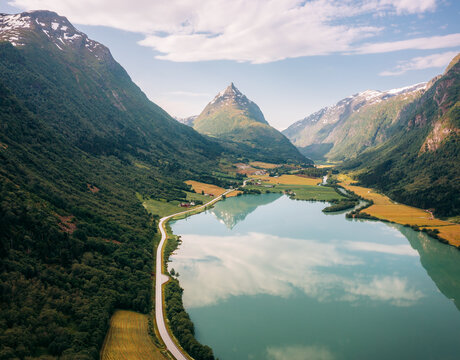 Aerial view of Eggenipa's peak reflected on the still lake below, surrounded by lush greenery and golden fields, Byrkjelo, Vestland, Norway.