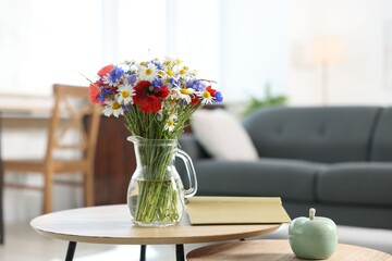 Beautiful wildflowers in vase and book on wooden table at home. Space for text