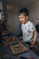 Smiling little boy in avocado print t-shirt stands in the kitchen near a cutting board with sliced...