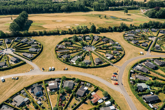 Aerial view of circular gardens with neat hedges and cozy homes, creating a vibrant green oasis against the golden fields, Br&Atilde;&cedil;ndby, Denmark.