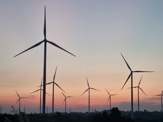 Wind Turbines at Sunset: A cluster of wind turbines stands silhouetted against a colorful sunset,...