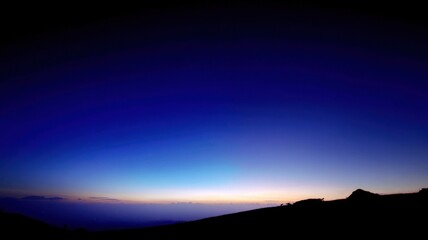 Obraz premium A twilight horizon with a dark blue sky transitioning to soft pink, orange, and yellow hues near the horizon,