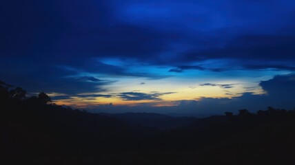 Fototapeta premium A twilight landscape with thick layers of clouds illuminated in shades of blue, orange, and yellow,