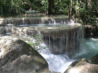 Obraz premium Cascade of Serenity: Captivating scenic view of a multi-tiered waterfall cascading down rocky steps, its waters flowing with graceful energy through a lush, natural, vibrant ecosystem.