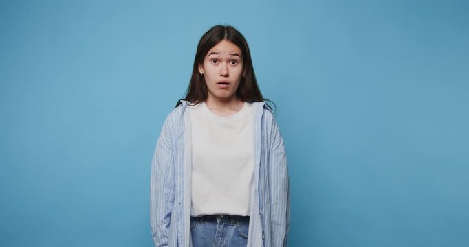 Expressive shocked young woman shares her feelings against a bright blue backdrop in a creative moment of self-reflection