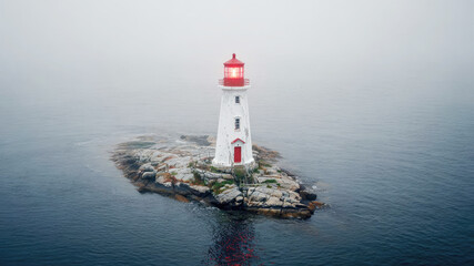 Lighthouse stands tall on rocky island surrounded by thick fog and calm waters at dusk