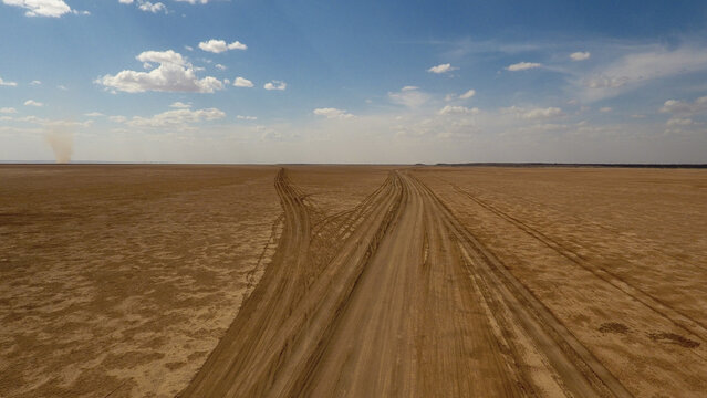 Aerial view of parallel tire tracks stretching across the vast, arid landscape under a bright, cloud-dappled sky, Marsabit, Marsabit County, Kenya.