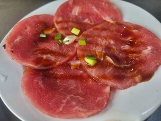 Exquisite Meat Slices Plated: A close-up shot of artfully arranged, thinly sliced, tender meat seasoned with a delicate sauce and finely chopped green herbs.