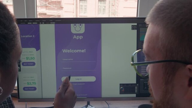 Over shoulder shot of male UX designer pointing computer screen displaying welcome page while discussing mobile app wireframe with Black female colleague in office space