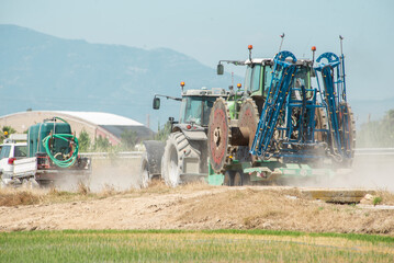 A large tractor towing farm machinery and irrigation equipment across a dry farm field on a sunny day in the heat. harvesting, farm machinery