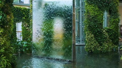 Biophilic design installation with indoor waterfall and lush vertical garden in a Bangkok shopping mall atrium surrounded by tropical plants, Thailand. Sustainability and wellness - Powered by Adobe
