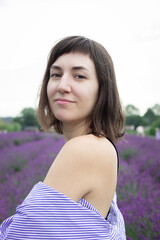 Beautiful 28-year-old brunette woman with bob haircut sitting in blooming lavender field on a summer day, peaceful mood, natural lifestyle