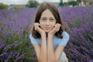 Portrait of a teenage girl sitting in a blooming lavender field. Peaceful summer scene with natural...