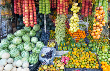 Fresh fruits grocery market in India, sale stall on street with burmese grapes, watermelon, apple and oranges, indian culture