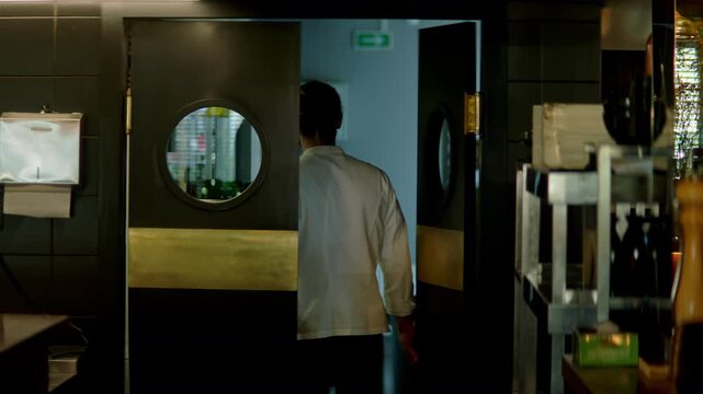 TRACKING Caucasian male chef walking out of commercial restaurant kitchen through the swinging doors. Shot with 2x anamorphic lens