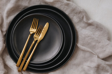 Golden cutlery rests on stacked black plates. Stylized tabletop scene evokes luxury dining. Editorial, design, and web use.