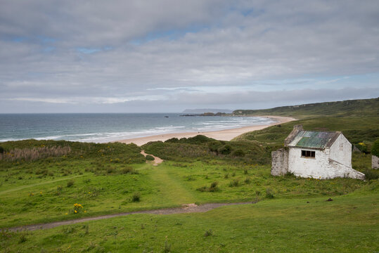 A panoramic view of White Park Bay, located on the Antrim Coast in Northern Ireland, featuring its sandy beach and rolling waves under a cloudy sky.