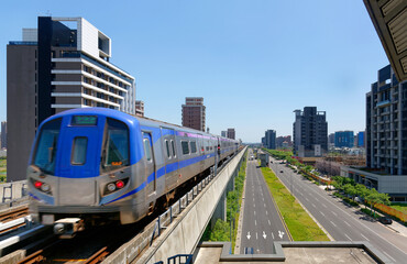 Fototapeta premium Scenic view of a metro train traveling on elevated rails of Taoyuan Mass Rapid Transit System (Taoyuan International Airport MRT System) under sunny blue sky in Chunli, New Taipei City, Taiwan