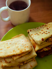 Delicious homemade crepes on a vibrant green plate paired with a steaming cup of tea, creating a cozy breakfast atmosphere