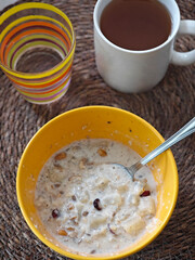 Morning delight of warm oatmeal with nuts and dried fruits alongside a steaming cup of tea and...
