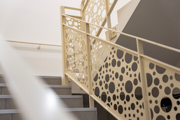 Vue sur un escalier intérieur de couleur crème, accompagné d’un garde-corps aux motifs ronds,...