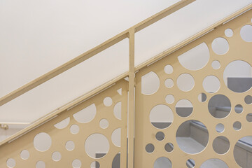 Vue sur un escalier intérieur de couleur crème, accompagné d’un garde-corps aux motifs ronds,...