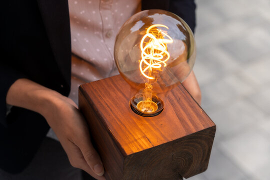 Innovative business idea presentation concept – corporate employee (woman) holding glowing lightbulb symbolizing creativity, startup energy, and visionary thinking in action