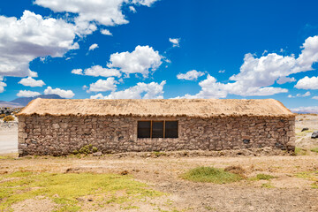 Amidst the Chilean Atacama Desert, a rustic stone hut with a straw roof provides shelter under a dramatic desert sky.