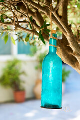 Close-up of a turquoise glass bottle hanging from a tree branch with rope, creating a rustic...