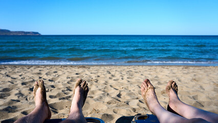 Couple relaxing on sandy beach with feet in the foreground, enjoying the view of the turquoise sea...