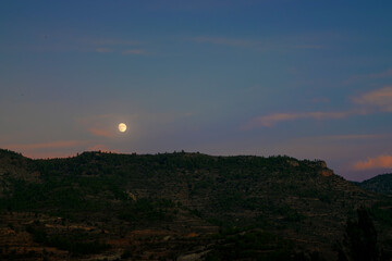 Mountain scene during nightfall with moon rising above the horizon
