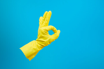 Right hand with yellow latex glove showing ok or  like sign on blue background