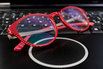 Glasses on a black laptop keyboard , soft focus side view close up
