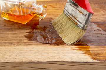 Sealing wood with linseed oil brush spread from a square bottle on oak wood texture, soft focus close up