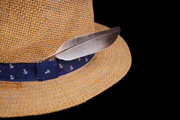Gray dove feather on a straw hat on black background, abstract summer vacation backdrop