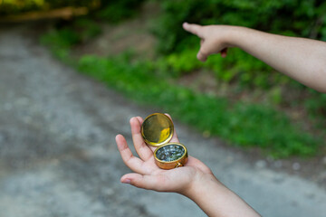 Male child hand holding a golden compass in the forest and pointing the way with index finger, soft focus close up with copy space