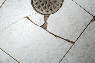 Clogged floor drain with broken ceramic tiles, obsolete bakdrop with cracks
