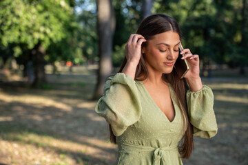 Stressed young woman talking on phone in park, visibly upset and worried about disturbing news...