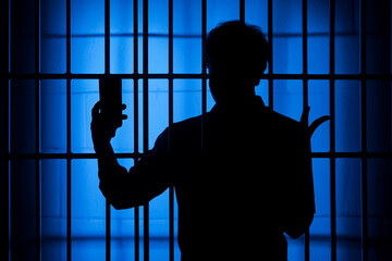 Silhouette of a person behind bars holding a phone blue background