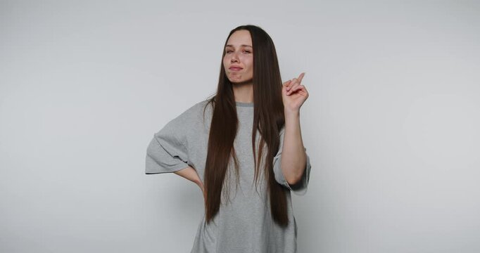 Young woman gestures playfully while looking thoughtful against a plain background she has an idea
