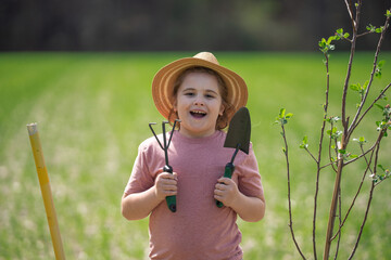 Kid with shovel in spring garden. Child cultivating a tree in garden.
