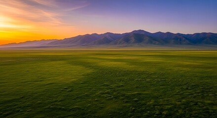 Obraz premium Green Grass Field Against Distant Mountains at Sunset
