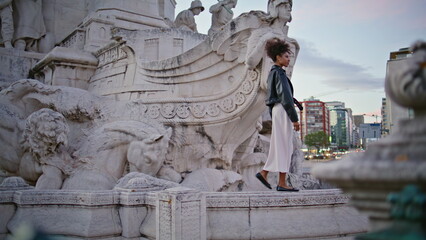 Woman standing historic sculpture at urban travel. Stylish african american lady