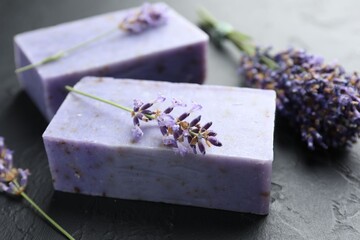 Aromatic soap bars and lavender flowers on dark textured table, closeup
