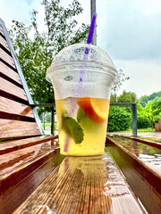 Glass of cold lemonade with orange, lemon and mint on a wooden bench on a rainy day