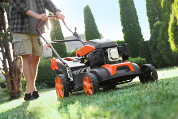 Man cutting green grass with lawn mower in garden, closeup