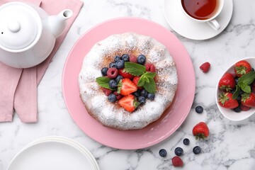 Tasty Bundt cake with powdered sugar and berries on white marble table, flat lay