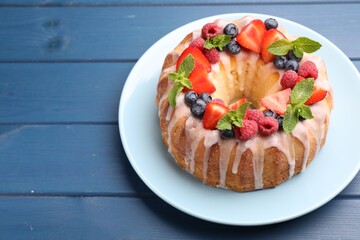 Delicious bundt cake with berries, glaze and mint on blue wooden table, closeup
